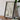 a framed map of a city or region, placed on a wooden surface next to a camera and some books.