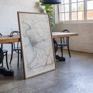 a large framed map of a region, with a wooden table and chairs in the background.