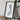 a framed map of Finland, placed on a wooden surface next to a camera and some books.