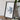 a framed map of Antarctica, placed on a wooden surface next to a camera and some books.