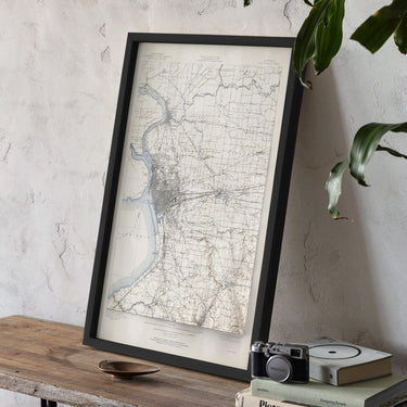 a framed map of a region, with a camera and some books placed on a wooden table in front of it.