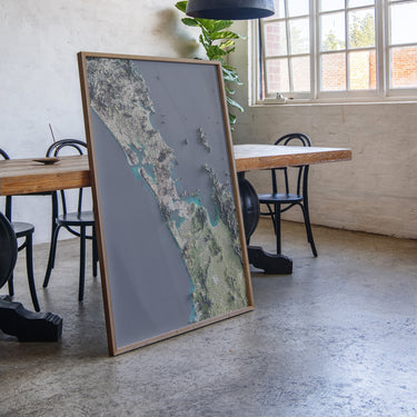 a large, framed map of New Zealand displayed in a room with a wooden table and chairs.