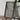 a framed aerial map of a region, with a camera and a book on a wooden table in front of it.