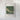 The image is a framed painting depicting a river or stream with a greenish-brown hue, surrounded by lush vegetation.