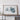 a large framed artwork depicting a blue and white abstract shape, placed on a wooden shelf against a white wall.