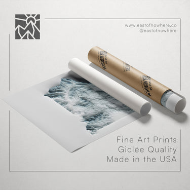 a roll of paper with a printed image of a wave, along with a tube of paper and a website address for fine art prints.