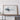 a large framed artwork depicting a stylized representation of a wave or sea creature, placed on a wooden shelf or table.