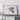 a large framed map of the world displayed on a wooden shelf against a white wall.