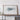 a large framed artwork depicting a mountain range, placed on a wooden shelf against a white wall.