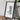 A framed map of a mountainous region is displayed on a wooden surface, accompanied by a camera and some books.