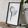 a framed map of South America, with a camera and books on a wooden table in front of it.