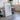 a large white framed artwork with a black border, standing on a wooden floor in a room with a window and a plant.