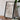 a framed map of the United States, with a camera and a book on a wooden table in front of it.