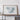 a large framed artwork depicting a map of a region, placed on a wooden shelf against a white wall.