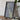 a framed map of New Zealand, placed on a wooden table next to a camera and some books.
