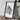 a framed map of a mountainous region, placed on a wooden surface next to a camera and some books.