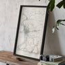 a framed map of a region, with a camera and some books placed on a wooden table in front of it.