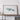 a large framed artwork depicting a landscape, placed on a wooden shelf against a white wall.