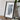 a framed map of Indiana, a black frame with a white border, placed on a wooden surface next to a camera and some books.