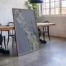 a large, framed map of New Zealand displayed in a room with a wooden table and chairs.