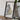 A framed map of England is displayed on a wooden table, with a camera and some books placed next to it.
