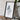 a framed map of a mountainous region, placed on a wooden surface next to a camera and some books.