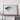 a large framed artwork depicting a mountain range, placed on a wooden shelf against a white wall.
