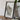 A framed map of Wisconsin is displayed on a wooden table, accompanied by a camera, a book, and some plants.