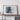 a large framed artwork of a mountainous landscape, displayed on a wall above a wooden table.
